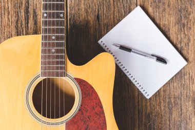 Akustik gitarın, Not Defteri kağıdının ve tahta zemin üzerindeki kalemin üst görünümü ve boşluğu kopyala