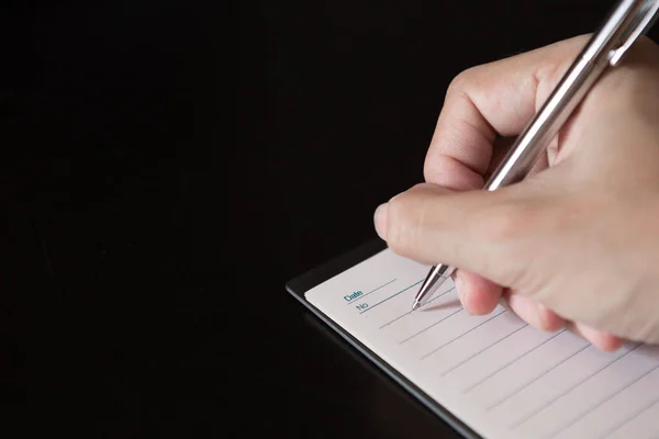 一只手拿着一支笔 在笔记本上黑色的背景和复制的空间上写字 — 图库照片
