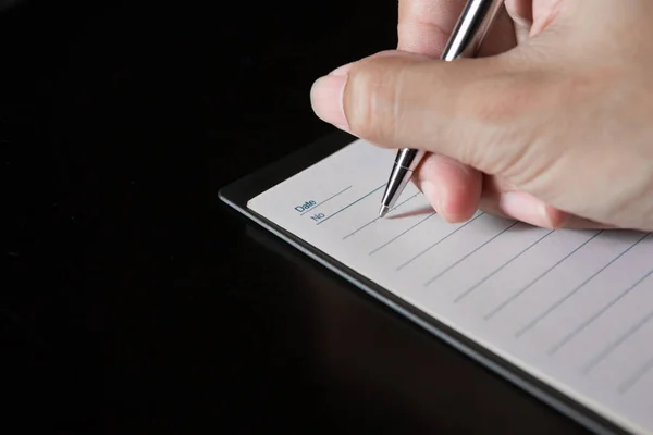 一只手拿着一支笔 在笔记本上黑色的背景和复制的空间上写字 — 图库照片