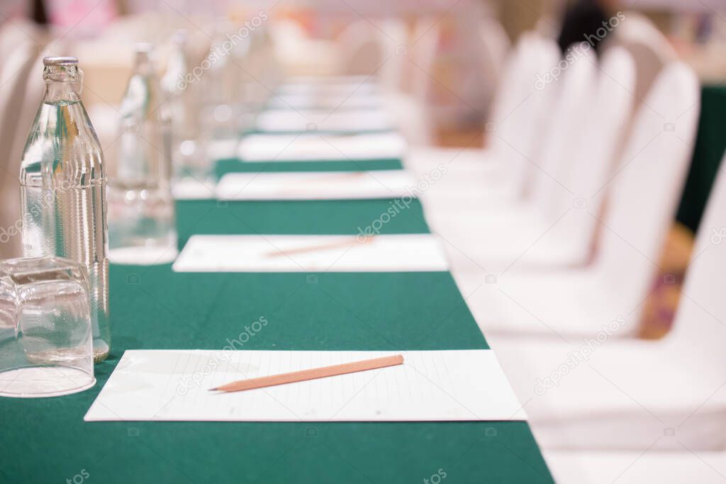 Selective focus of Paper, pencil, water bottle, glass on the table in the seminar room background