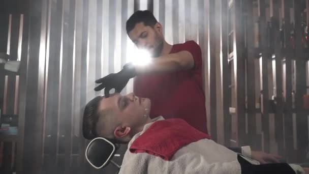 Barber in a red T-shirt and black gloves shaves the gangster.