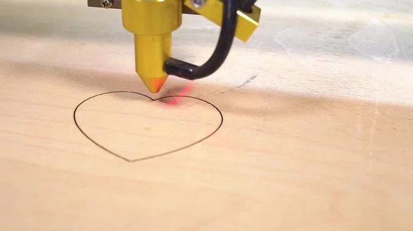 Laser engraving wood machine cut heart on yellow plywood.