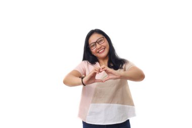 Güzel Asyalı kız elleriyle bir kalp işareti oluştururken ayakta duruyor. Beyaz arkaplanda izole