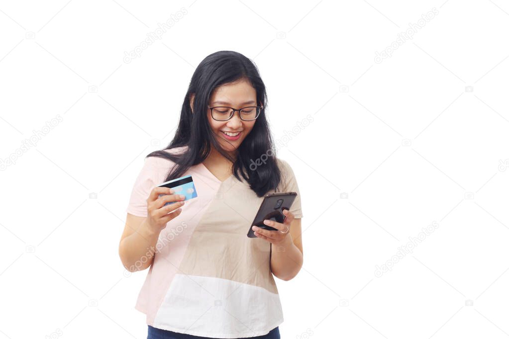 Beautiful girl from Asia smiles happily seeing good news on a smartphone while holding a credit card. The concept of online shopping. Isolated against a white background with copyspace