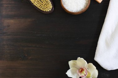 Kadın vücudu ve cilt bakımı, banyo ve spa ürünleri, kaptaki deniz tuzu, beyaz havlu, güzel çiçek, siyah ahşap zeminde kuru masaj fırçası. Güzellik, kozmetik. Kopyalama alanı ile yatay