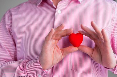 Eli kırmızı kalbe bağlı gömlekli bir adam göğsünün cebine yakın bir yerde.