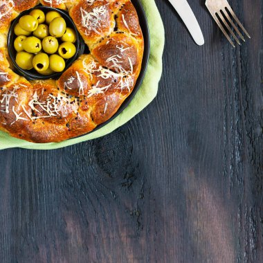 Lezzetli turta, dolgun çörekli yuvarlak maymun ekmeği rendelenmiş peynir ve siyah susam kasesiyle kaplanmış yeşil zeytinler siyah masada, bıçak ve çatal zeytinyağı fotokopi alanı ile.