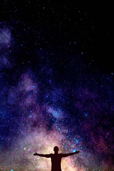 Samanyolu 'yla parlak gökyüzünün altında elleri açık bir adamın karanlık silueti. Kartpostal, duvar kağıdı veya tasarım için boşluk kavramı, metin için kopyalama alanı arkaplanı olan dikey