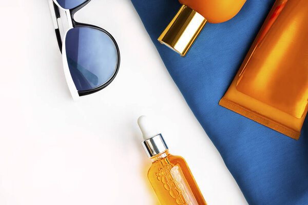 Orange mock up bottles of sun screen and sunglasses on bright contrast blue beach wrap on horizontal empty white background with copy space. Holiday flat lay