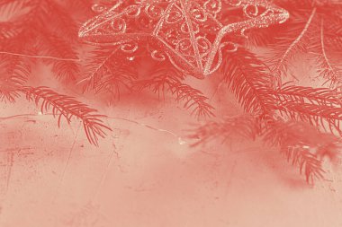 Kürk konisi, altın yıldız ve gri arka planda peri ışıkları olan Noel ağacı dalları. Kopya uzayı ile yatay. Tatillerde ve partilerde otel ve restoran rezervasyonu. Mercan duotonu