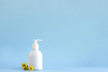 Kozmetik ve malzemelerle ilgili tasarım için fotokopi alanı olan açık mavi arka planda şifalı bitki örtüsü ya da Tussilago farfara içeren beyaz plastik model şişe dağıtıcısı.