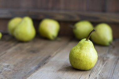 Arka planda çözünmüş armutlar olan desenli ahşap kahverengi masa üzerinde taze yeşil armut. Seçici odaklanma. Kopya uzayı ile yatay. Tarım, meyve ve sağlıklı gıda tasarımı için.