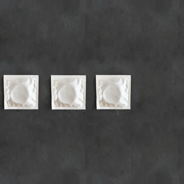 Řada tří fólií šedý čtverec modelovat kondom balení na prázdném černém křídovém pozadí s kopírovat prostor ochrany zdraví Hiv, pohlavně přenosné nemoci a nechtěné těhotenství. Horní pohled — Stock fotografie