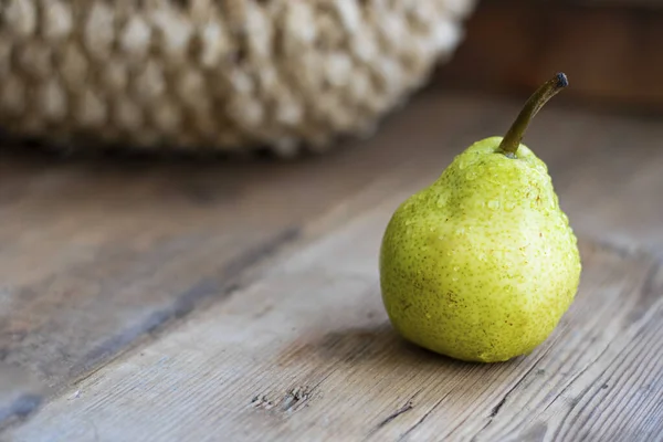 fresh green pear on rustic wooden brown table with defocused pears in basket on background. Selective focus. Horizontal with copy space for design about agricilture, fruit, healthy food