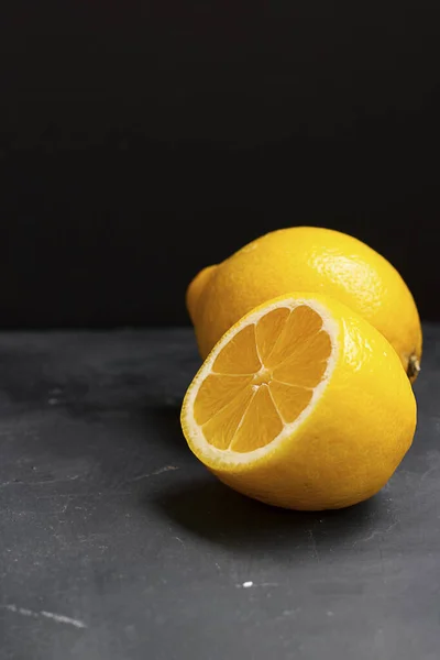 Half of lemon in focus and whole lemon behind on a black plain background