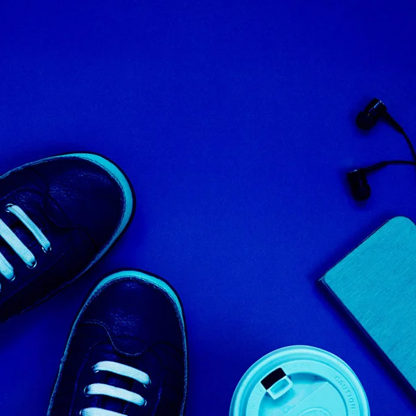 Sports flat lay with coffee, sell phone, sneakers and earphones on blank background. Classic, blue monochrome, trend 2020