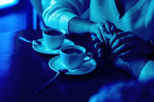 Hombre y mujer tomados de la mano, primer plano de las parejas brazos en la mesa de madera en el restaurante con dos tazas. fecha en la cafetería, relaciones, amor, matrimonio, día de San Valentín, regalo. Clásico, azul monocromo, tendencia 2020 — Foto de Stock