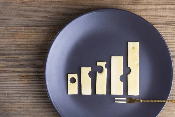 Business growth and food concept of increase graphs made of cheese on plate with fork on wooden texture. Growing up trend, Economy, Agriculture and dairy manufacture. Horizontal, copy space. Top view.