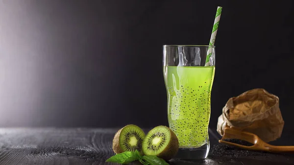 Frisches grünes veganes Getränk im Glas mit Stroh mit Kiwi und Basilikumkernen für Gesundheit auf schwarzem Bachgrund mit Kopierraum, vegetarisches Essen, dunkler Schlüssel. Konzept von natürlichem Coctail und Saft. Detox. — Stockfoto