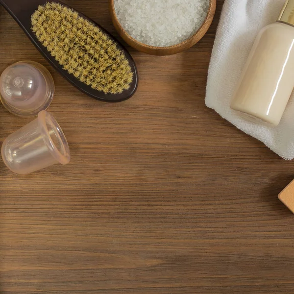 Kadın vücudu ve cilt bakımı, banyo ve spa ürünleri, kaptaki deniz tuzu, mochup şişesi, beyaz havlu, kuru masaj fırçası ve kahverengi ahşap arka plandaki silikon süpürgeler. Üst Manzara. Kopyalama alanı olan kare.