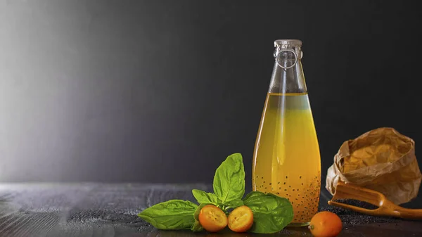 Fresh orange vegan beverage in bottle with cumquat and basil seeds for health on black bachground with copy space, vegetarian food, dark key. Detox. Concept of natural coctail and juice.