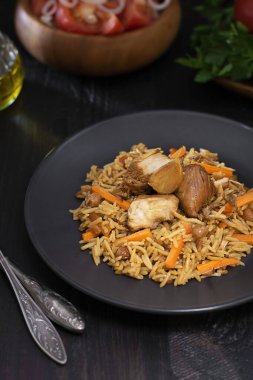 Geleneksel pilav, siyah tabakta hindi ile koyu ahşap masa üzerinde çözünmüş salata, domates, yeşillik ve yağ. Doğu, Özbek yemekleri etten yapılır ve yükselir. Dikey.