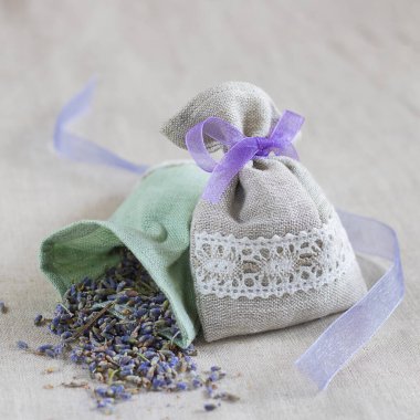 Small linen bag filled with dried lavender decorated with lacework and violet ribbon coque, two sachets, one is opened. Square. Composition on thenatural flaxen background. clipart