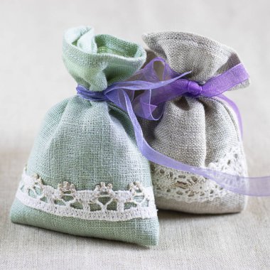 Two small linen sacks filled with dried lavender decorated with lacework and violet ribbon coque, aroma sachet. Square. Closeup composition on the natural flaxen background. clipart