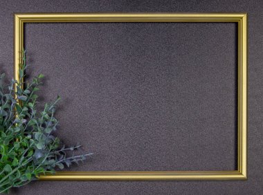 Dekoratif kompozisyon, gri arka planda altın fotoğraf çerçevesi, yapraklı dallar. Düz konum, üst görünüm, kopyalama alanı.