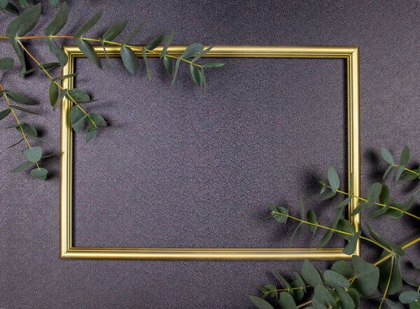 Decorative composition, golden photo frame on a gray background, branches with leaves. Flat lay, top view, copy space.