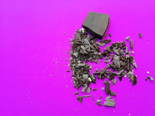 Small uneven bar of dark brown chocolate with large chips on a bright lilac background