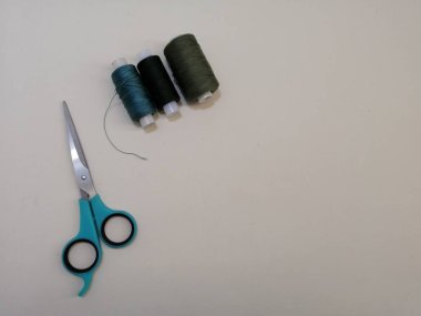 Sol arka planda beyaz bir makas ile koyu yeşil iplik yeni makara