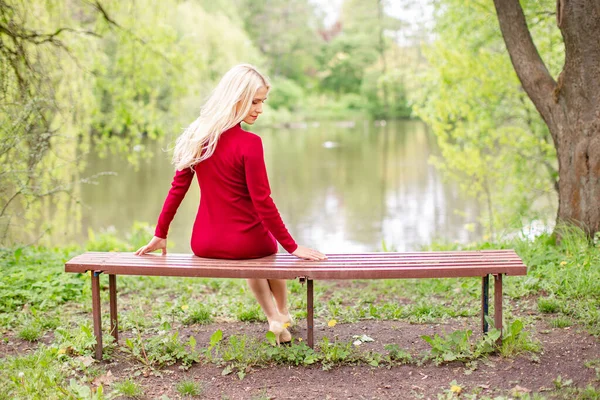 Blond woman wearing an office clothes sitting on a bench in the park near a lake. The picture reflects the return to natural life
