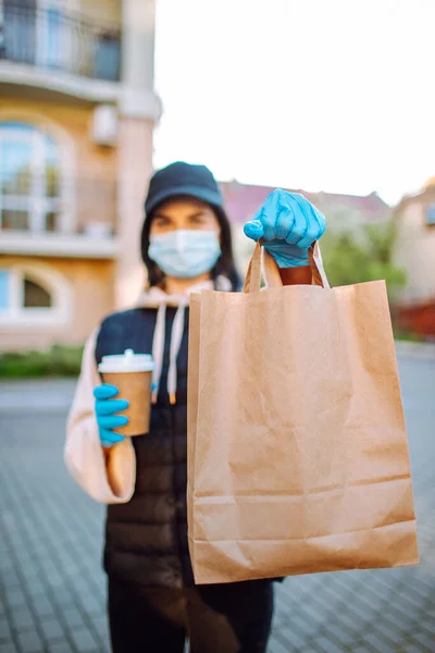 Health protection, safety and pandemic concept - delivery woman in protective face mask and gloves with a bag of food and coffee. Selective focus