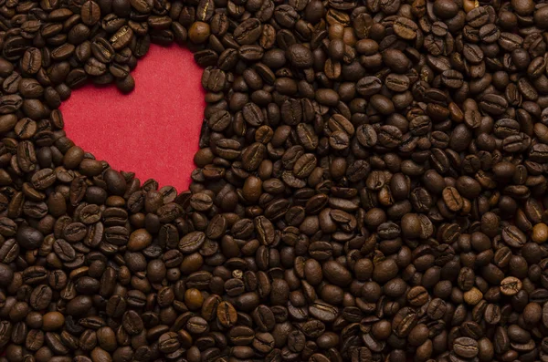 Красное сердце из кофейных зерен на фоне кофе — стоковое фото