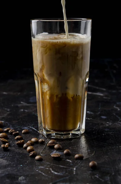 Café gelado em um copo com leite derramando em fundo preto — Fotografia de Stock