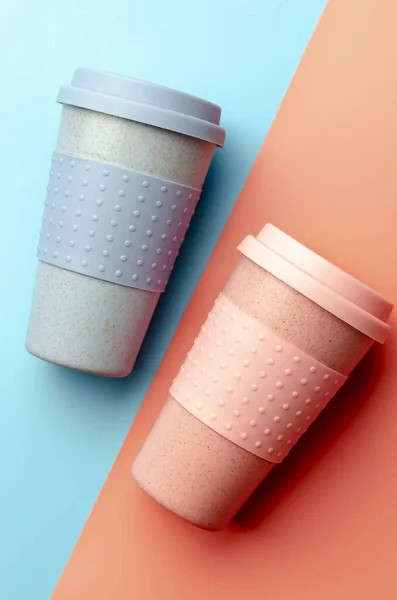 Reusable bamboo coffee cup with silicone holder on colorful background. Flat lay, copy space.