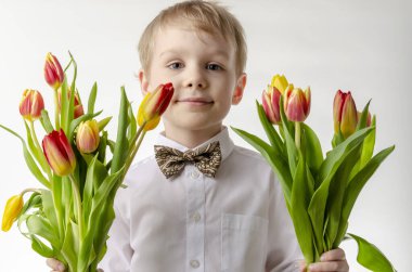 Elinde bir buket çiçek tutan sevimli bir çocuk. Laleler. Anneler Günü. Uluslararası Kadınlar Günü. Beyaz arka planda mutlu küçük bir çocuğun portresi..