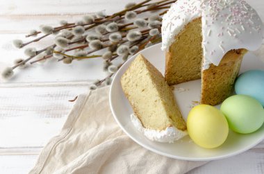 Beyaz ahşap arka planda beyaz jöleli renkli yumurtalı Kulich Paskalya pastası