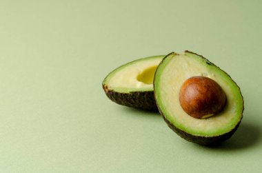 Pastel yeşil arka planda yarım avokado. Basit bir minimalizm ve nesneler