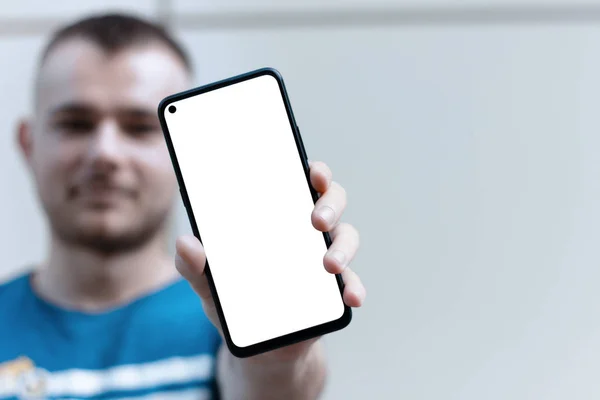 Akıllı telefonunu beyaz ekranla gösteren genç bir adam. Bulanık arka plan odaklı ön kamerası olan akıllı telefon boş ekran. Uygulama ve web sitesi tasarımı için model.