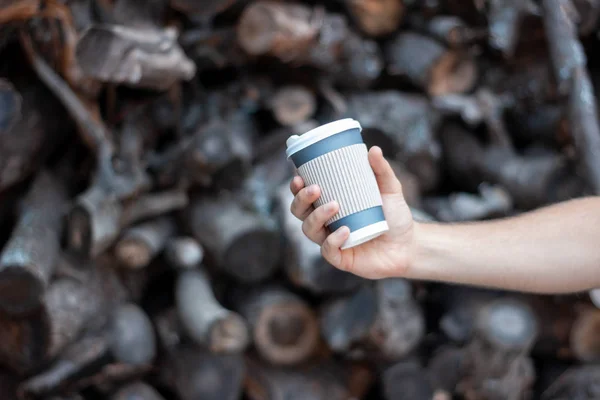 Hand with a take-away coffee on the background of sawn logs. Plastic cup on the background of the damage to the environment. Save the planet, no plastic.
