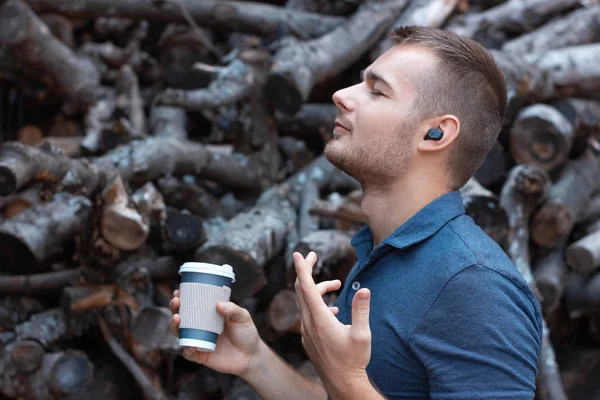 Modern bir genç adam, kablosuz kulaklıklarıyla müzik dinliyor ve elinde bir kahve tutuyor. Kulaklıklarda bluetooth kulaklıklar. 