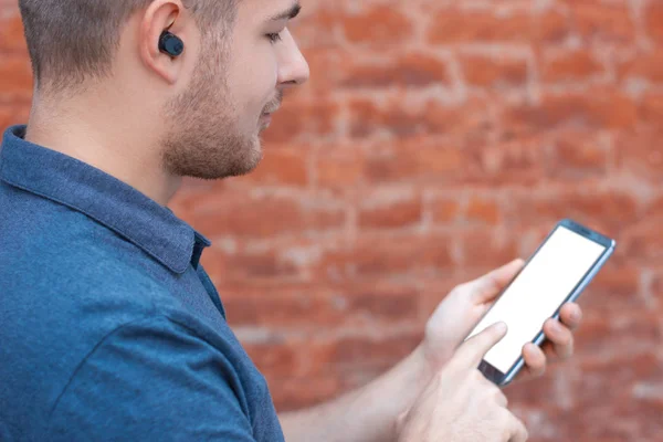 Genç adam kablosuz kulaklıkla müzik dinliyor ve beyaz ekranlı akıllı telefonu tutuyor. Müzik albümü tasarım kapağı, mobil uygulama ya da web sitesi için hazırlan. Arkadan bak. Teknoloji uzmanına ayak uydurmak.. 