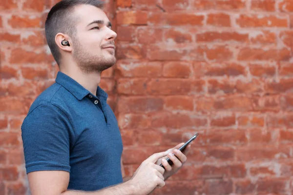Modern man listening music by bluetooth earphones. Guy control wireless headphones from his smartphone. Keeping up with technology person. Empty space