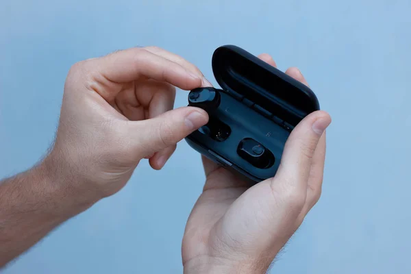 Gri arka planda beyaz bir adamın elinde siyah kablosuz kulaklıklar. Bir durumda bluetooth kulaklıklar.