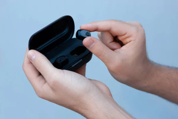 Gri arka planda beyaz bir adamın elinde siyah kablosuz kulaklıklar. Bir durumda bluetooth kulaklıklar.