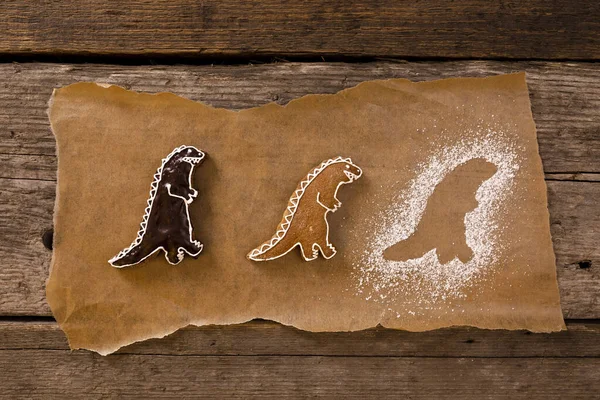 Zelfgebakken peperkoek in de vorm van dinosaurussen op bruin bakpapier op oude houten ondergrond. Rechtenvrije Stockfoto's