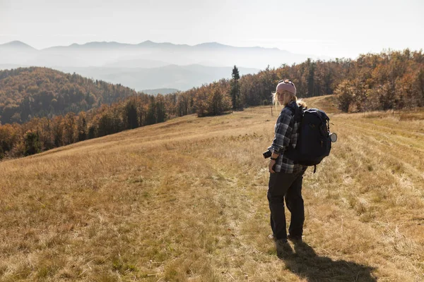 Donna sorridente in berretto con zaino escursionismo in montagna — Foto Stock