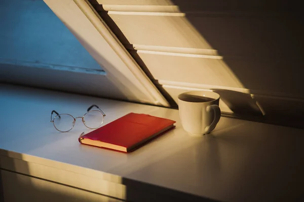 Projektowanie wnętrz sypialnia lub pokój dzienny z przytulnym stylu w świetle popołudniowym, czerwony notatnik, szklanki i filiżanka kawy na białym drewnianym gabinecie. — Zdjęcie stockowe